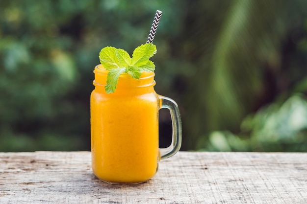 Smoothie à la mangue dans un pot Mason en verre et mangue sur fond vert. Shake à la mangue. Notion de fruits tropicaux