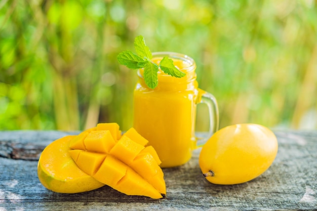 Photo smoothie de mangue dans un pot en verre mason et mangue sur le vieux fond en bois mango shake concept de fruit tropical