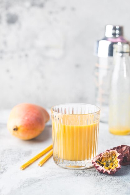 Smoothie à la mangue tropicale dans un verre et mangue fraîche sur fond clair. Shake à la mangue. Notion de fruits tropicaux.