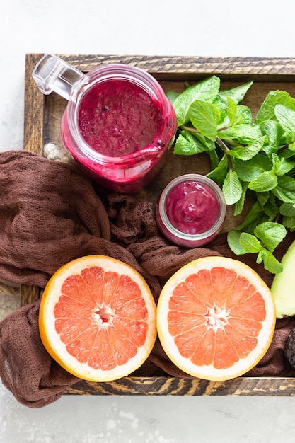 Smoothie pourpre avec myrtilles fraîches, menthe, avocat et pamplemousse dans un plateau en bois. La nourriture saine. Petit déjeuner ou déjeuner d'été.