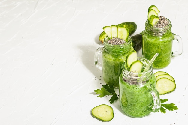Smoothie vert au concombre dans un bocal en verre. Légumes mûrs frais, légumes verts et graines de chia. Lumière dure à la mode, ombre sombre. Fond de mastic blanc, espace de copie