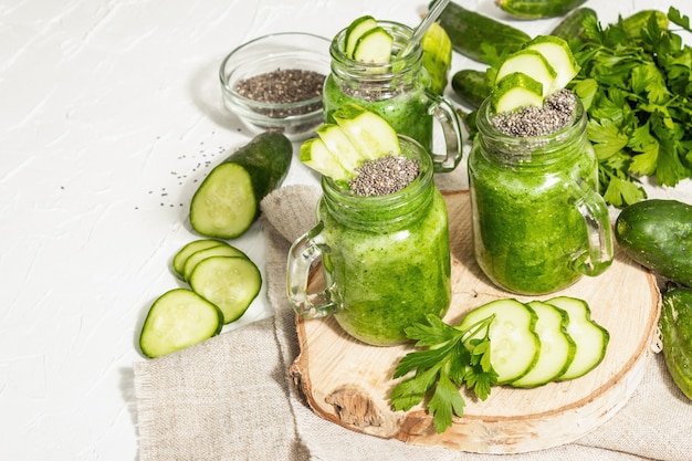 Smoothie vert au concombre dans un bocal en verre. Légumes mûrs frais, légumes verts et graines de chia. Lumière dure à la mode, ombre sombre. Fond de mastic blanc, gros plan