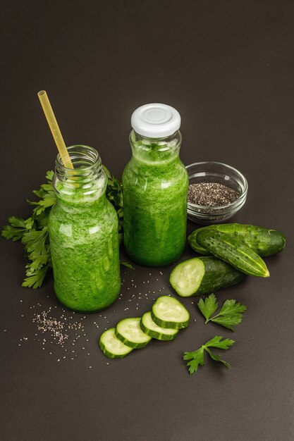 Smoothie vert au concombre dans des bouteilles en verre. Légumes mûrs frais, légumes verts et graines de chia. Fond de béton de pierre noire, gros plan