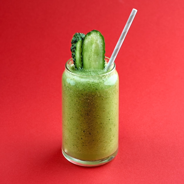 Smoothie vert au concombre sur une surface rouge