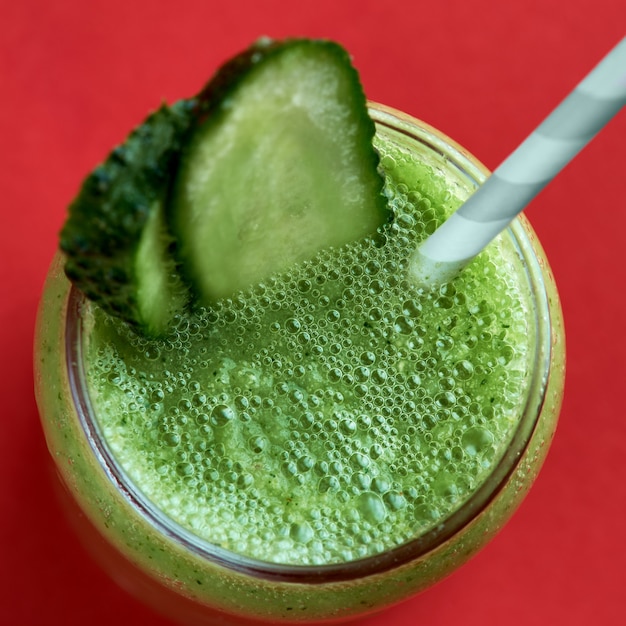 Smoothie vert au concombre sur une surface rouge