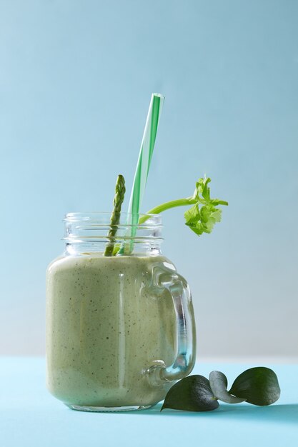 Smoothie vert aux asperges et légumes biologiques verts de céleri dans un bol en verre sur bleu duotone