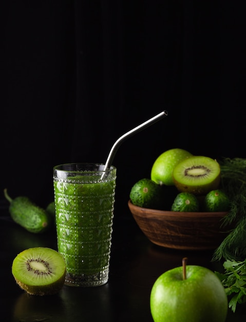 Smoothie vert dans un verre en verre sur fond noir. Kiwi, pommes, concombres et légumes verts. Cuisiner des aliments sains. Zero weist, un tube en métal.