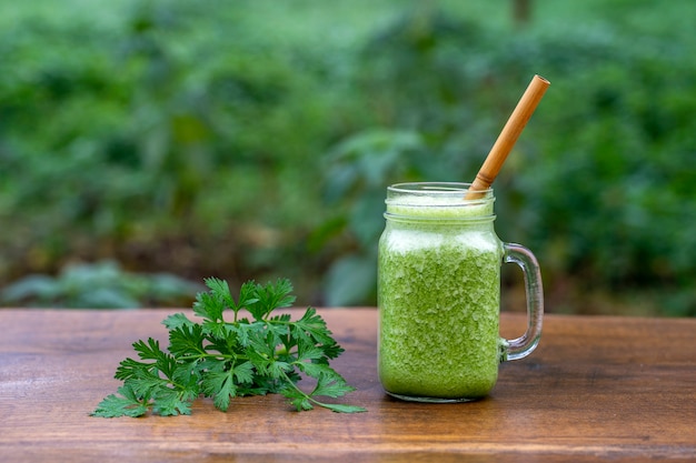 Smoothie vert de persil, avocat, miel et banane dans une tasse en verre sur une table en bois dans un café de jardin, gros plan. Concept d'alimentation saine