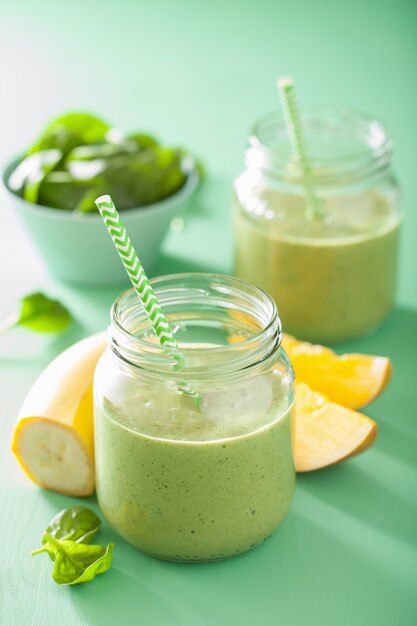 Smoothie vert sain avec banane mangue épinards dans des bocaux en verre