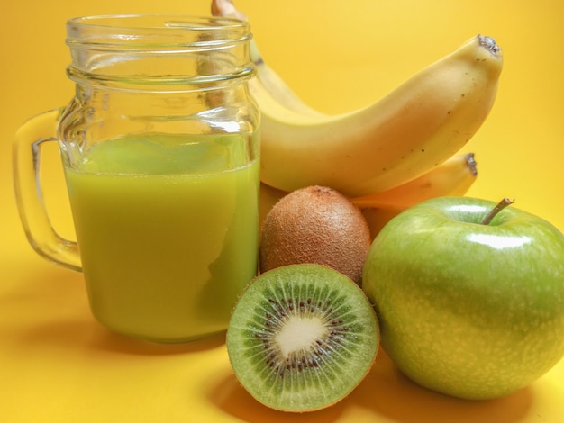 Smoothie vert sain en pot de verre: banane, kiwi, pomme verte. Boisson saine sur fond jaune.