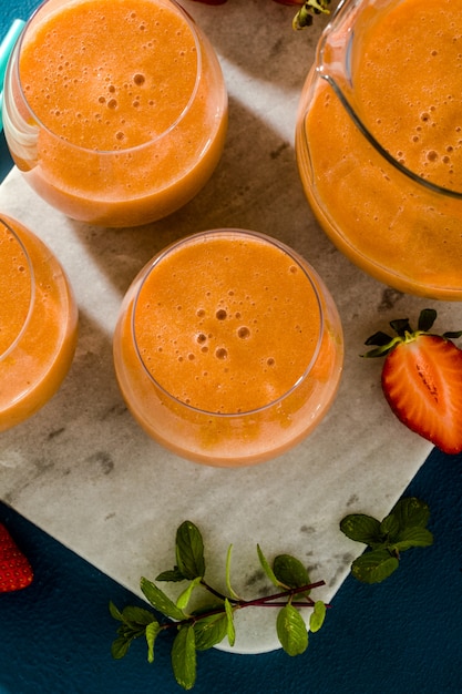 Smoothies aux fraises dans une carafe et verres sur fond bleu. petit déjeuner cru