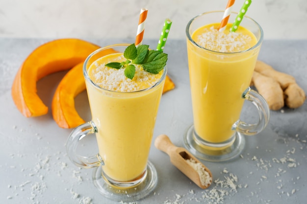 Smoothies à la citrouille avec des copeaux de gingembre et de noix de coco et de menthe dans un verre sur fond de pierre claire ou de béton Boisson saine et délicieuse pour le petit déjeuner