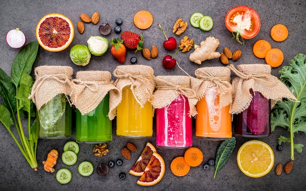 Smoothies et jus sains colorés en bouteilles avec des fruits tropicaux frais et des superaliments sur pierre sombre