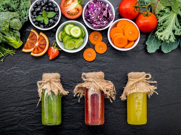 Smoothies et jus sains colorés dans des bouteilles avec des fruits tropicaux frais sur fond de pierre sombre.