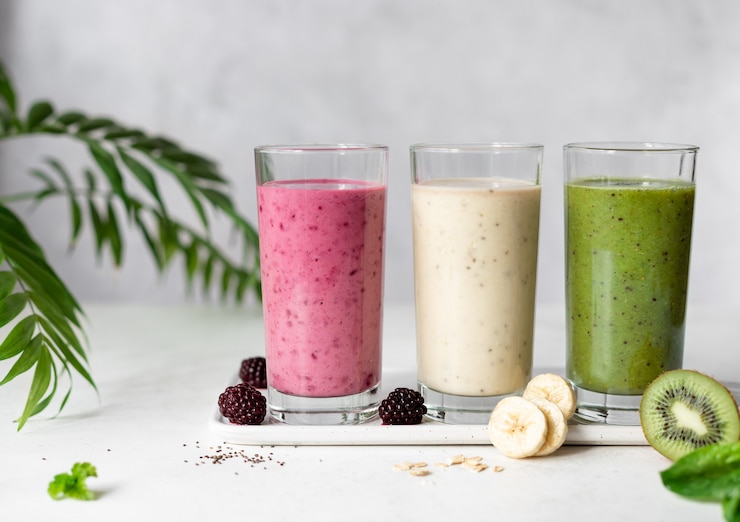 Photo smoothies végétaliens colorés avec mûres, banane et flocons d'avoine, kiwi et épinards concept alimentaire végétalien fond gris avec des feuilles de palmier horizontal, copie espace,
