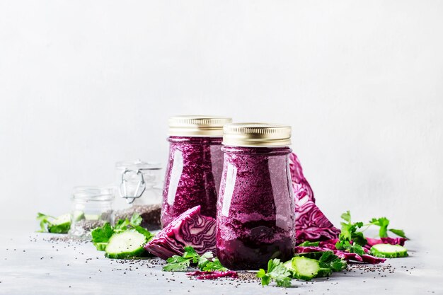 Smoothies violets détox végétaliens sains ou jus de concombres de chou rouge avec graines de chia dans des bouteilles en verre sur fond gris mise au point sélective