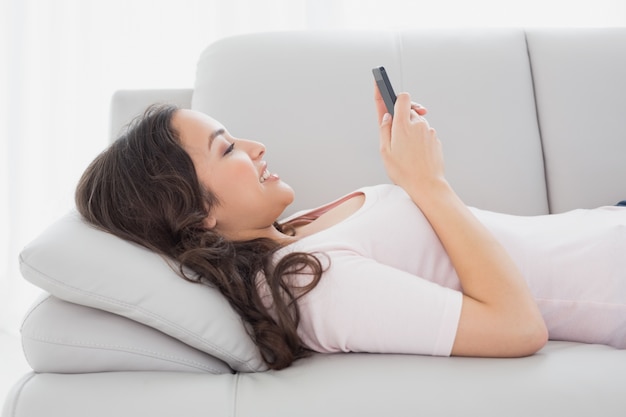 SMS souriant de jeune femme sur le canapé à la maison