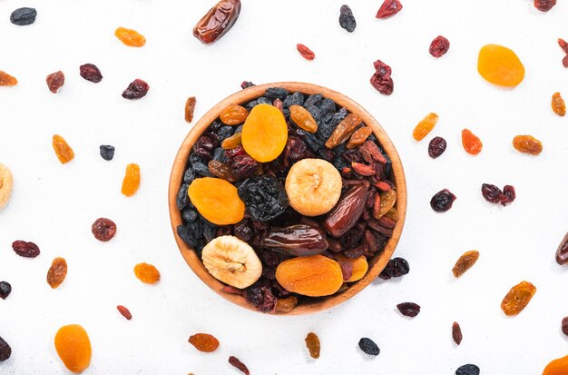 Snack-alimentaire sain fruits secs naturalxUn mélange biologique séché au soleil d'abricots secs figues raisins secs dattes canneberges cerises baies de goji pruneaux dans des bols sur fond blanc vue de dessus