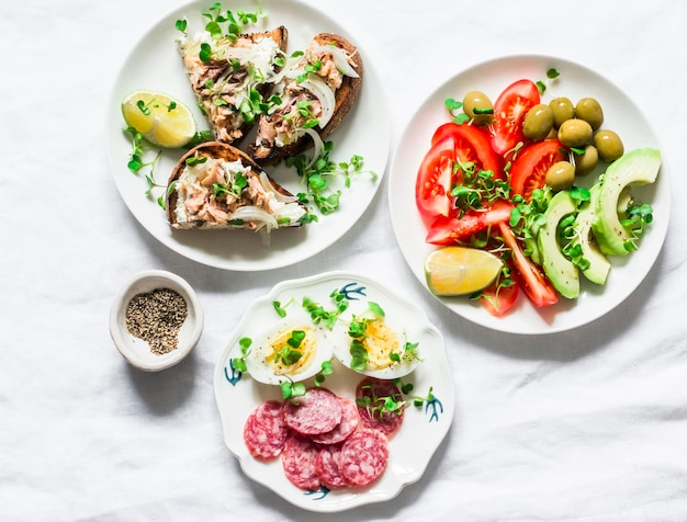 Snack apéritifs tapas table de petit déjeuner salami maquereau fromage à la crème sandwichs olives avocat tomates micro verts sur fond clair vue de dessus