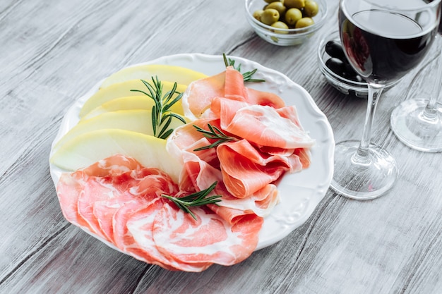 Snack appétissant prosciutto italien avec melon, olives et un verre de vin