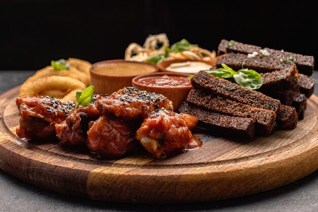 Snack à la bière sur une planche de bois rondelles d'oignon croûtons calamars ailes de poulet grillées et sauces