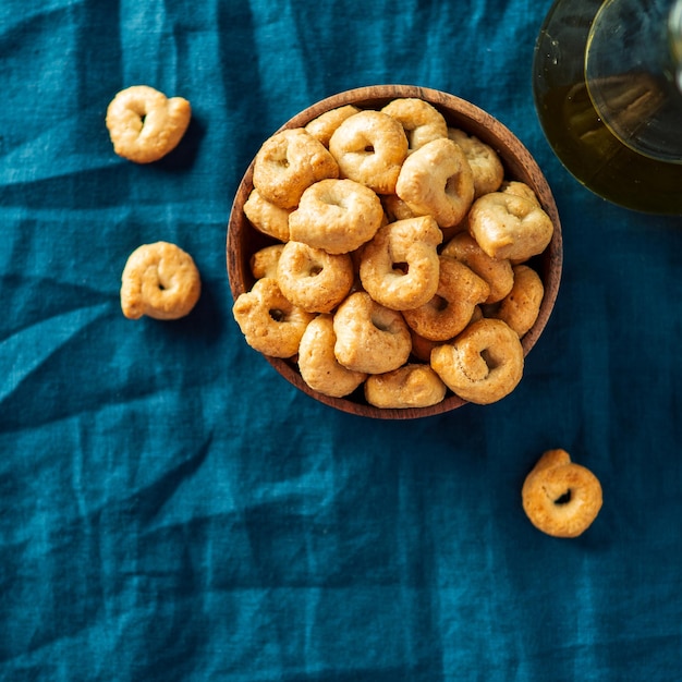 Snack italien traditionnel taralli ou tarallini dans un bol en bois sur un fond de serviette de lin bleu foncé Aperitif rustique de taralli avec espace de copie Vue supérieure ou à plat Crop carré