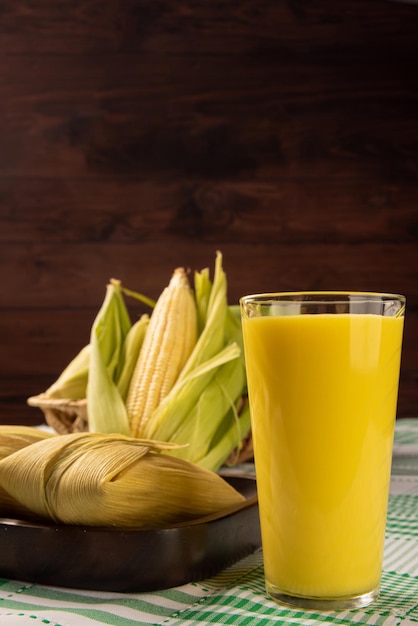 Snack-maïs brésilien maïs pamonha et jus de maïs disposés sur une table avec nappe verte et blanche fond sombre mise au point sélective