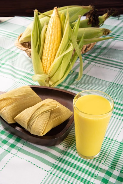 Snack-maïs brésilien maïs pamonha et jus de maïs disposés sur une table avec nappe verte et blanche fond sombre mise au point sélective