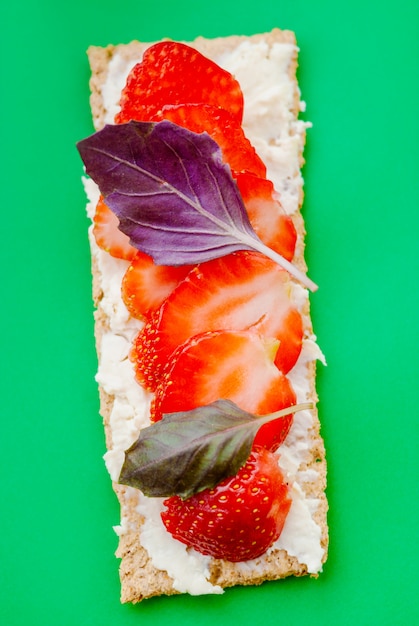 Snack avec pain croustillant, fromage à la crème, fraise et basilic sur fond vert