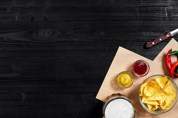 Snack pour chips de fête nachos avec sauces tomate ketchup moutarde et chope de bière sur fond noir...