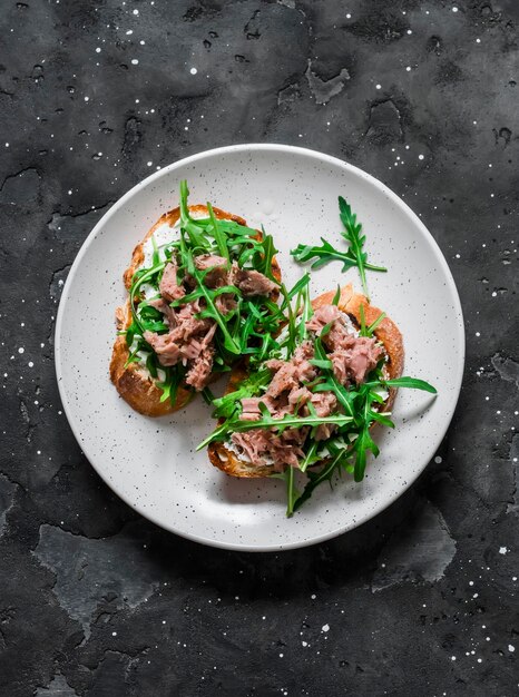 Snack-sandwichs avec du fromage à la crème de thon en conserve et de la roquette sur une vue de dessus de fond sombre