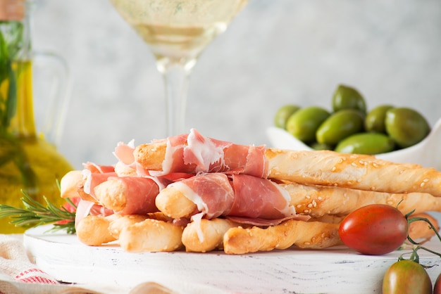 Snacks italiens traditionnels pour le vin, les gressins (grissini), les tomates, le prosciutto (jamon), les fraises et les olives. Mise au point sélective, gros plan