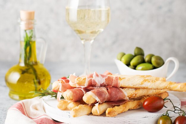 Snacks italiens traditionnels pour le vin, les gressins (grissini), les tomates, le prosciutto (jamon), les fraises et les olives. Mise au point sélective.