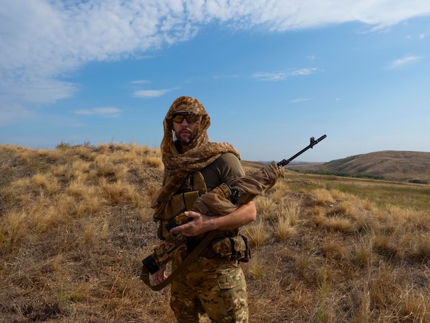 Snipermercenaire en tenue de camouflage sous le soleil brûlant, il se tient debout avec un fusil et examine le