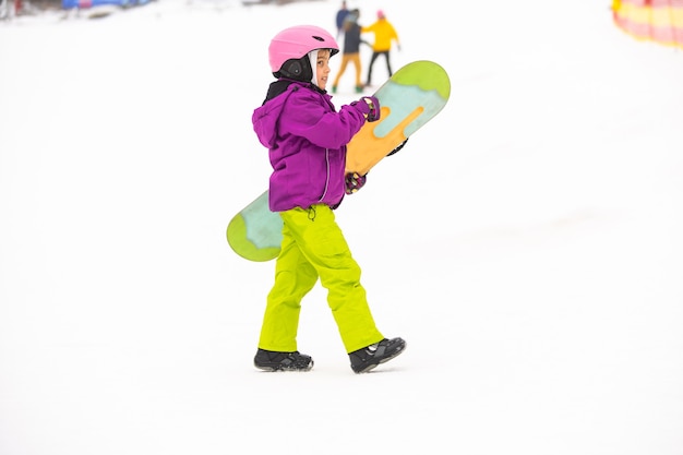 Photo snowboard sports d'hiver. petite fille apprenant à faire du snowboard, portant des vêtements d'hiver chauds. fond d'hiver.