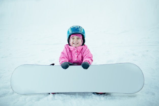 Photo snowboard winter sport. petite fille enfant jouant avec de la neige portant des vêtements d'hiver chauds.