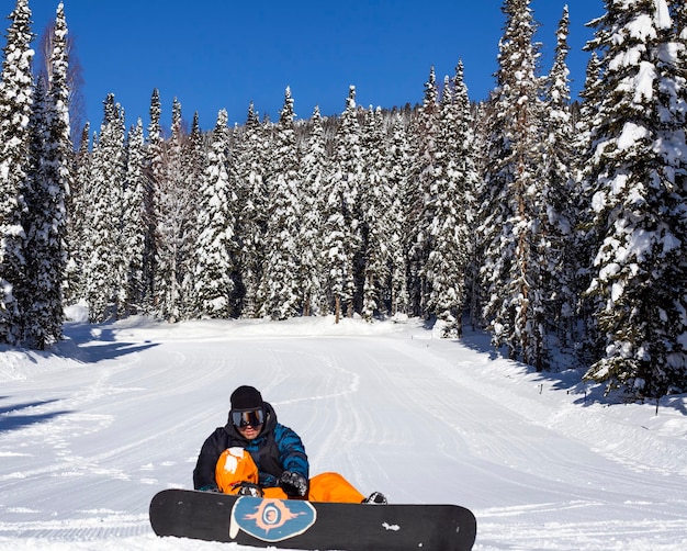 snowboarder est assis sur la neige dans la forêt. Focus sur la forêt