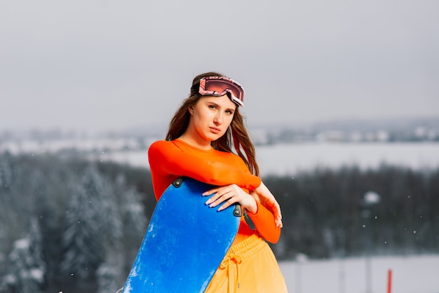 Snowboarder fille heureuse posant dans des lunettes de soleil avec un snowboard