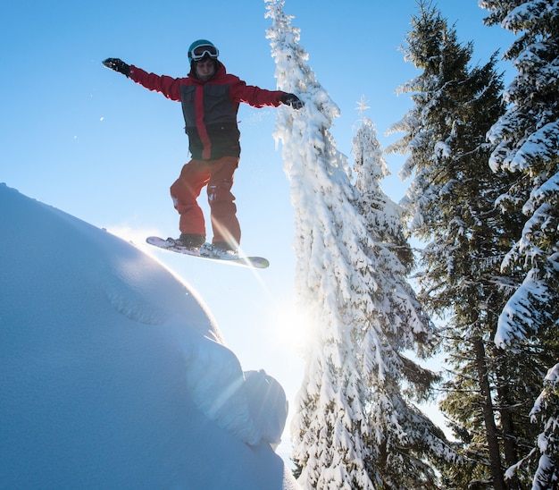 Snowboarder freerider sautant dans les airs tout en surfant sur la pente dans les montagnes. Ciel bleu et soleil. Concept de saison de ski et de sports d'hiver