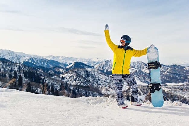 Snowboarder de jeune femme dans une veste jaune et un casque noir sur le fond des montagnes enneigées