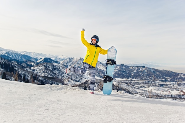 Snowboarder de jeune femme dans une veste jaune et un casque noir sur le fond des montagnes enneigées