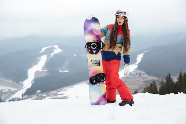 Snowboarder de jeune femme sur les pentes journée d'hiver glaciale tenant le snowboard dans les mains