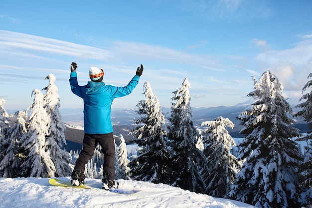 Snowboarder a levé les bras et les mains vers le ciel à la station de ski, l'homme a grimpé au sommet d'une montagne à travers