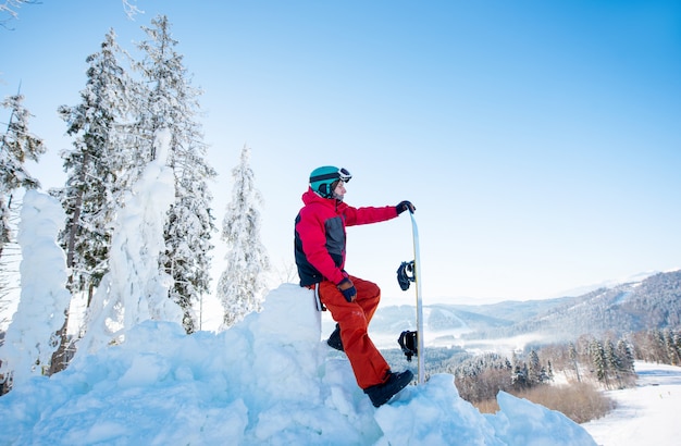 Snowboarder mâle reposant au sommet d'une pente
