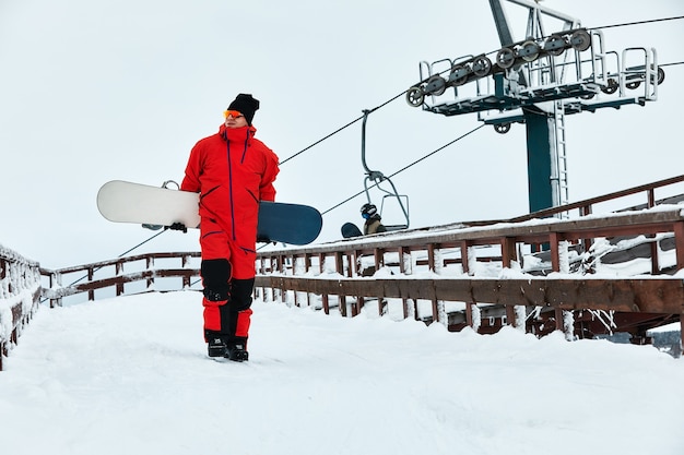 Snowboarder masculin dans un costume rouge marchant sur la colline enneigée avec concept de snowboard, de ski et de snowboard.