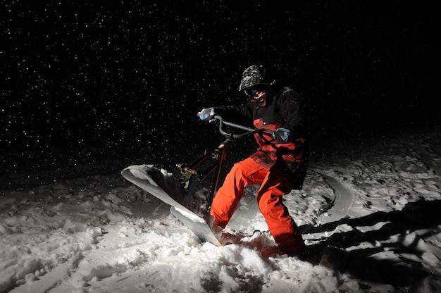 Snowboarder en orange sportswear sautant sur une colline enneigée la nuit