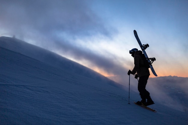 Un snowboarder en raquettes escalade une montagne d'hiver avec un snowboard sur ses épaules