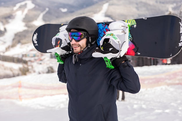 Photo snowboarder relaxant et posant à la journée ensoleillée sur ske resort avec snowboard au-dessus de la tête. l'heure d'hiver.