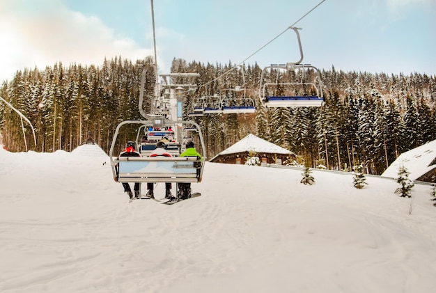 Snowboarder et skieurs montent sur un téléski jusqu'à une montagne enneigée par une journée ensoleillée avec une forêt enneigée