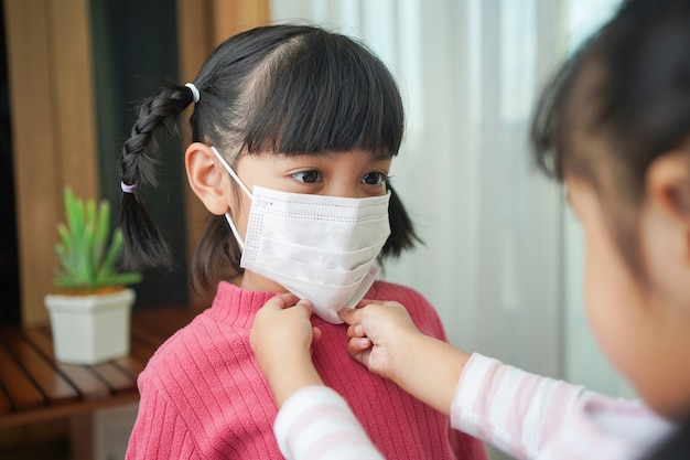 La sœur aide la jeune fille à mettre le masque chirurgical. Prévention de l'infection par le coronavirus ou l'infection Covid-19